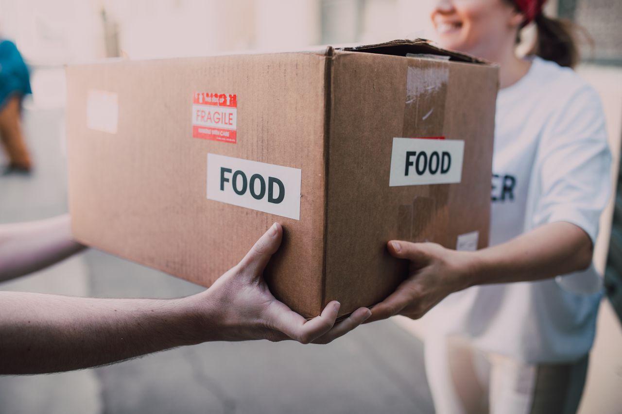 Hands exchanging a box labeled Food, symbolizing charity and support.